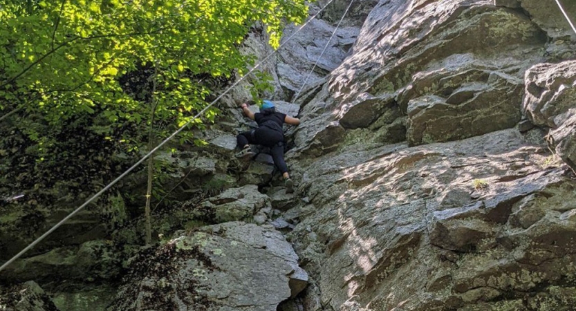 A person wearing safety gear is secured by ropes as they climb a rock wall. 